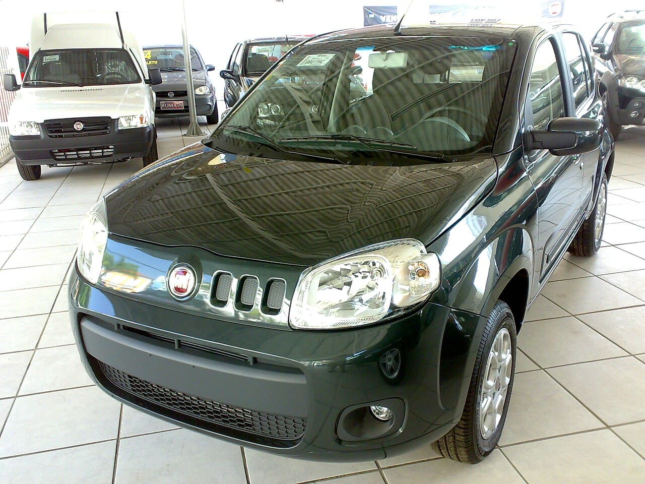 Fiat Novo Uno verde-escuro de quatro portas, visto de três quartos dianteiro em pátio de concessionária